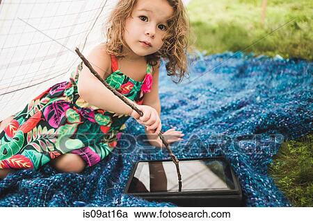 Stock Image - Girl in homemade garden tent using twig on digital tablet screen. Fotosearch