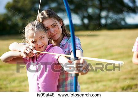 Stock Image - Girl learning archery from teenage sister. Fotosearch