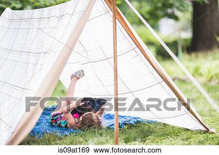 Girl lying on back in homemade garden tent looking at digital tablet View Large Photo Image Stock Photo - Girl lying on back in homemade garden tent looking at digital tablet. Fotosearch