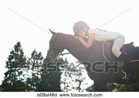 Stock Image - Girl on horseback leaning forward to pet horse. Fotosearch