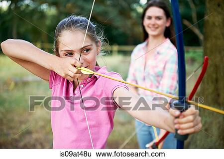 Girl practicing archery aiming with bow and arrow View Large Photo Image Stock Photograph - Girl practicing archery aiming with bow and arrow. Fotosearch