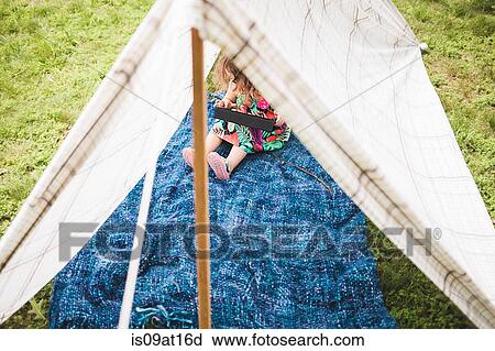 Stock Image - Girl sitting in homemade garden tent using digital tablet. Fotosearch