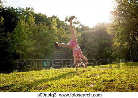 Stock Image - Girl upside down doing cartwheel looking at camera. Fotosearch