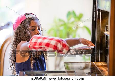Stock Photo - Girl wearing oven glove inserting cake tins into oven. Fotosearch