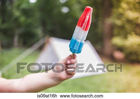 Stock Image - Hand of girl holding ice lolly in garden. Fotosearch