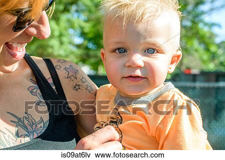Head and shoulders of tattooed mother holding baby boy looking at camera View Large Photo Image Stock Photo - Head and shoulders of tattooed mother holding baby boy looking at camera. Fotosearch