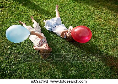 Stock Image - High angle view of brother and sister lying on grass holding balloon. Fotosearch