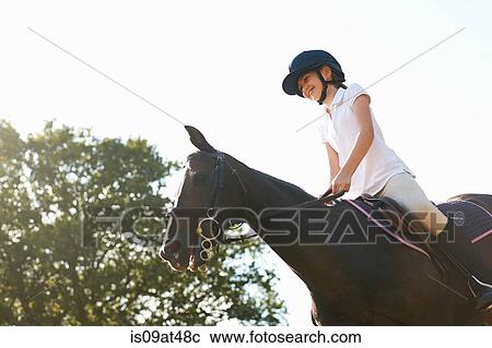 Stock Image - Low angle view of girl riding horse in countryside. Fotosearch