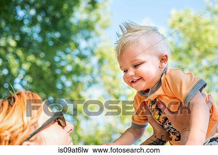 Stock Photo - Low angle view of mother holding up smiling baby boy. Fotosearch