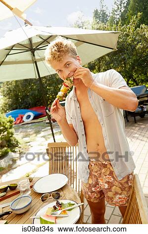 Man biting into kebab at party View Large Photo Image Stock Photograph - Man biting into kebab at party. Fotosearch