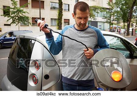 Stock Image - "Man charging electric car on street, Paris, France". Fotosearch