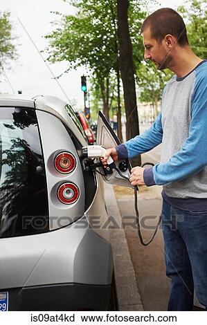 Stock Image - "Man charging electric car on street, Paris, France". Fotosearch