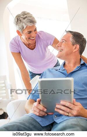 Mature couple chatting whilst using digital tablet View Large Photo Image Stock Photograph - Mature couple chatting whilst using digital tablet. Fotosearch