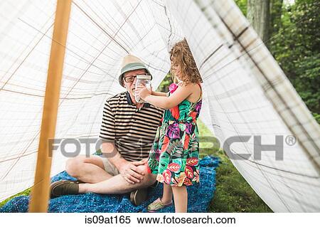 Stock Photography - Mature man with granddaughter holding insect jar in homemade garden tent. Fotosearch