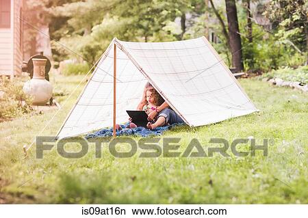 Picture - Mature woman and granddaughter sitting in homemade garden tent looking at digital tablet. Fotosearch