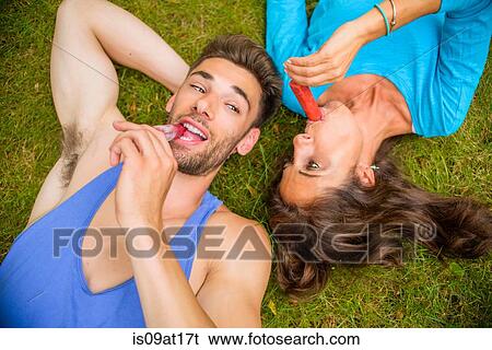 "Mature woman and young man, lying on grass, eating ice lollies, overhead view" View Large Photo Image Stock Photograph - "Mature woman and young man, lying on grass, eating ice lollies, overhead view". Fotosearch