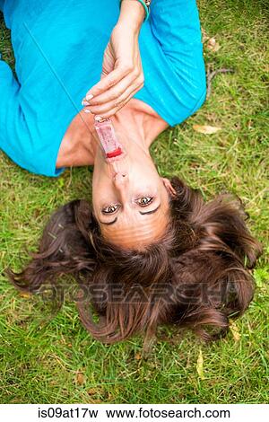 "Mature woman lying on grass, eating ice lollies, overhead view" View Large Photo Image Stock Photo - "Mature woman lying on grass, eating ice lollies, overhead view". Fotosearch