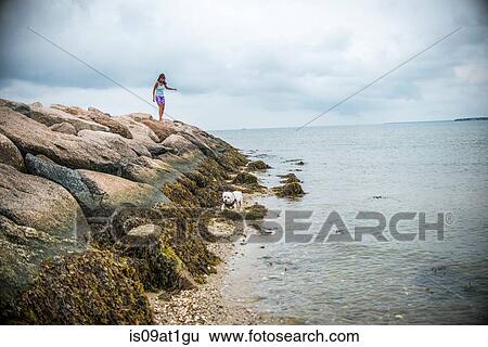 Stock Photograph - "Mature woman stepping over coastal rocks, Cape Cod, USA". Fotosearch