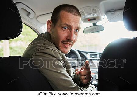 Stock Photo - "Mid adult man sitting in car, leaning over to back seat, pointing". Fotosearch