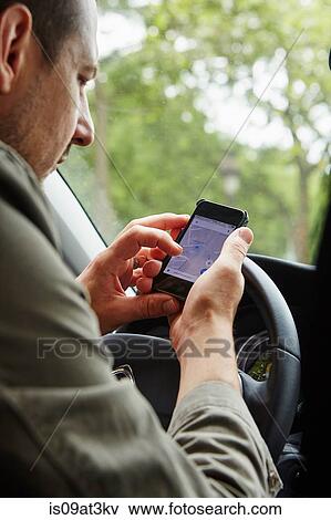 Stock Photo - "Mid adult man sitting in car, looking at map on smartphone". Fotosearch