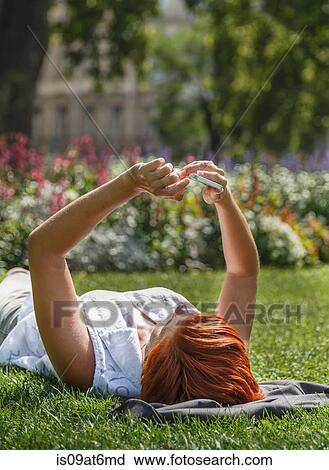 Mid adult red haired woman lying on grass using smartphone View Large Photo Image Stock Image - Mid adult red haired woman lying on grass using smartphone. Fotosearch