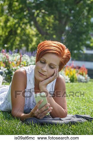"Mid adult red haired woman on grass resting on elbow, chin in hand using smartphone" View Large Photo Image Stock Image - "Mid adult red haired woman on grass resting on elbow, chin in hand using smartphone". Fotosearch
