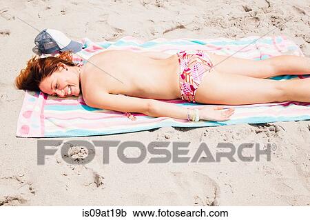 Stock Image - Mid adult woman lying on beach. Fotosearch