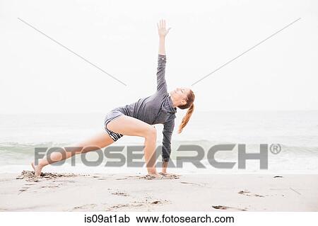 Stock Image - "Mid adult woman meditating on beach, rear view". Fotosearch