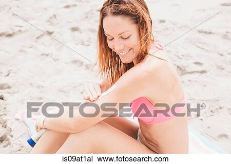 Stock Image - "Mid adult woman on beach, applying sunscreen". Fotosearch