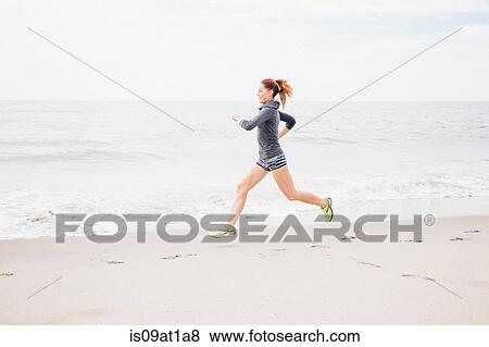 Stock Photo - Mid adult woman running along beach. Fotosearch