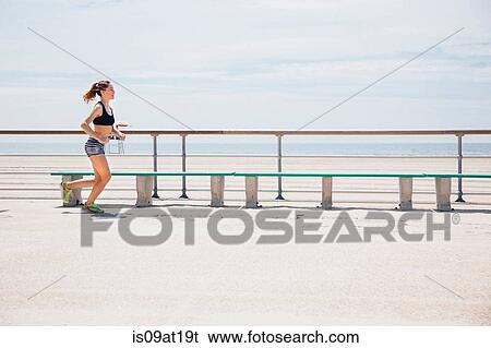 Stock Photograph - Mid adult woman running beside beach. Fotosearch