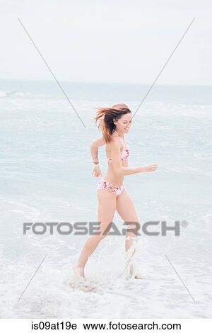 Stock Image - Mid adult woman running in sea. Fotosearch