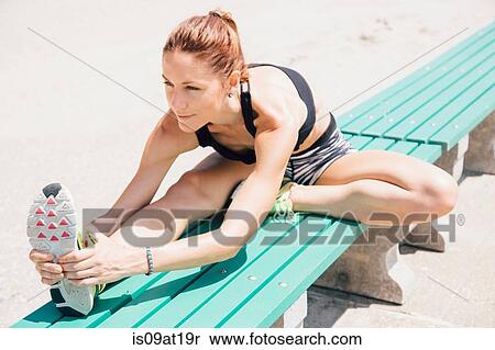 Stock Photography - "Mid adult woman sitting on bench, stretching". Fotosearch