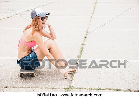 Picture - Mid adult woman sitting on skateboard. laughing. Fotosearch