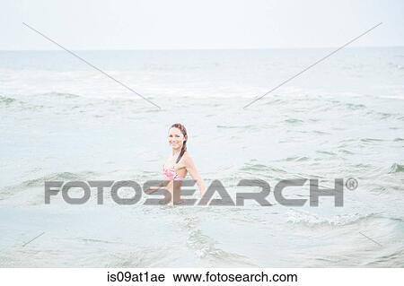 Stock Image - Mid adult woman standing in sea. Fotosearch
