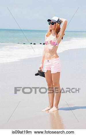 Picture - "Mid adult woman standing on beach, looking at view". Fotosearch