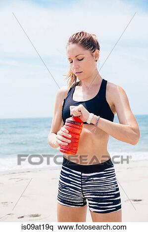 "Mid adult woman standing on beach, unscrewing cap from drinks bottle" View Large Photo Image Stock Photography - "Mid adult woman standing on beach, unscrewing cap from drinks bottle". Fotosearch