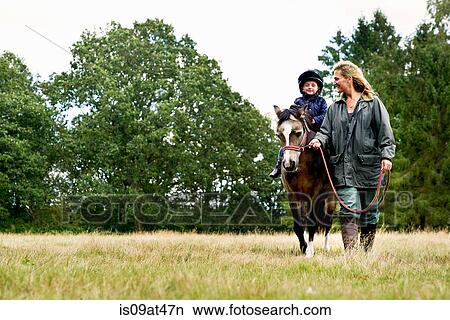 Picture - Mother leading horse riding son in field. Fotosearch