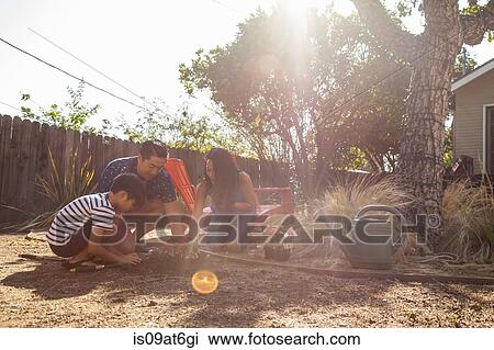 Stock Image - Parents and son planting in sunlit garden. Fotosearch