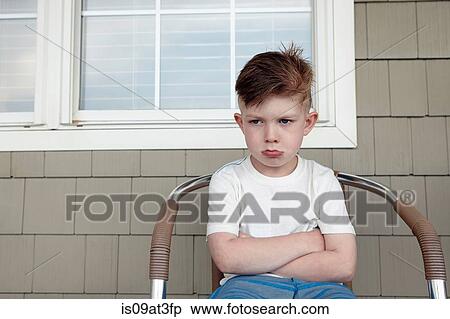 Stock Photography - Portrait of boy sitting outside house sulking. Fotosearch