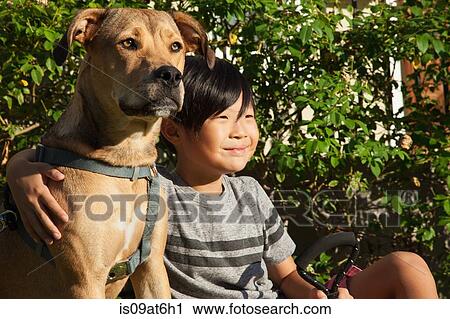 Stock Image - Portrait of boy with arm around dog in garden. Fotosearch