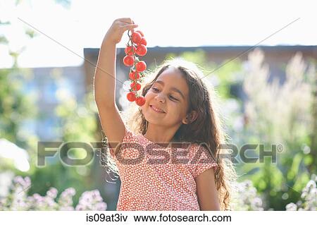 Stock Photo - Portrait of girl holding up bunch of cherry tomatoes in garden. Fotosearch