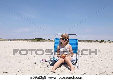 Portrait of girl wearing sunglasses sitting on deck chair at beach View Large Photo Image Stock Photo - Portrait of girl wearing sunglasses sitting on deck chair at beach. Fotosearch