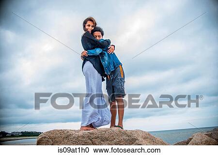 Stock Image - "Portrait of mature woman and son hugging on coastal rocks, Cape Cod, USA". Fotosearch