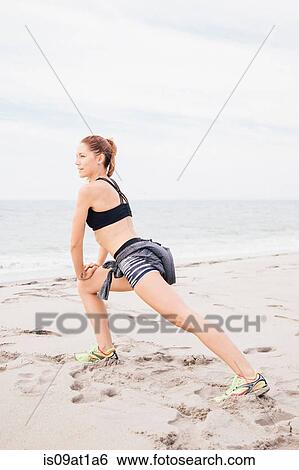 Stock Photograph - Portrait of mid adult stretching on beach. Fotosearch