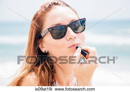 "Portrait of mid adult woman on beach, wearing sunglasses, applying lipstick" View Large Photo Image Stock Image - "Portrait of mid adult woman on beach, wearing sunglasses, applying lipstick". Fotosearch