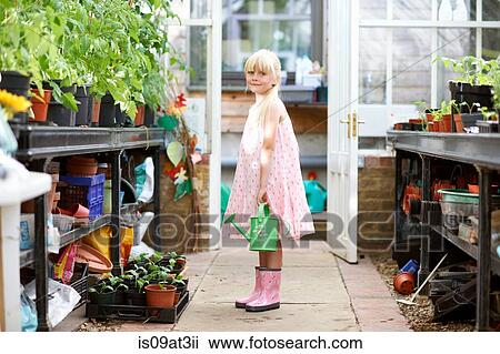 Portrait of pretty girl holding watering can in greenhouse View Large Photo Image Stock Image - Portrait of pretty girl holding watering can in greenhouse. Fotosearch