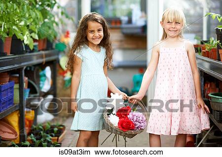 Picture - Portrait of two girls holding basket of fresh flowers in greenhouse. Fotosearch
