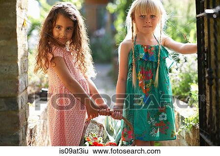 Stock Photograph - Portrait of two girls holding basket of fresh tomatoes in garden. Fotosearch