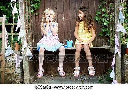 Portrait of two girls sitting on bench eating a bucket of fresh strawberries View Large Photo Image Stock Photo - Portrait of two girls sitting on bench eating a bucket of fresh strawberries. Fotosearch